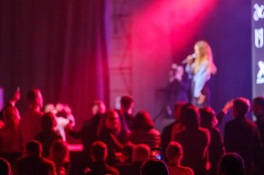 Dramatik sahne ışıkları altında seyirciye hitap eden konuşmacı heyecan verici bir atmosfer yaratıyor