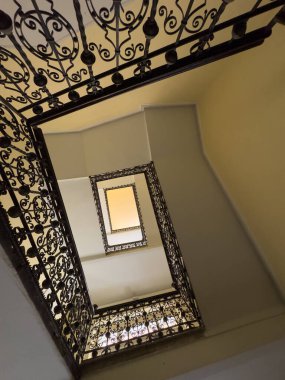 Karmaşık demir parmaklıklar ve sıcak ışıklandırmayla sarmal merdiven manzarası mimari ilgi yaratıyor.