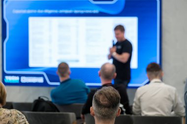 Konferans ortamında iş konularını sunan konuşmacıları dikkatle dinleyen izleyiciler.