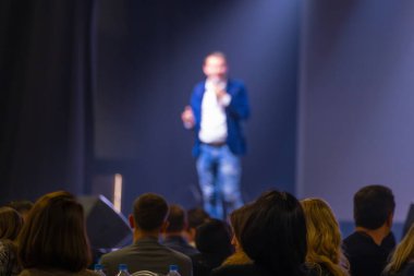 Sunum sırasında sahne ışıkları altındaki bir konferansta iş dünyasına seslenen bulanık konuşmacı