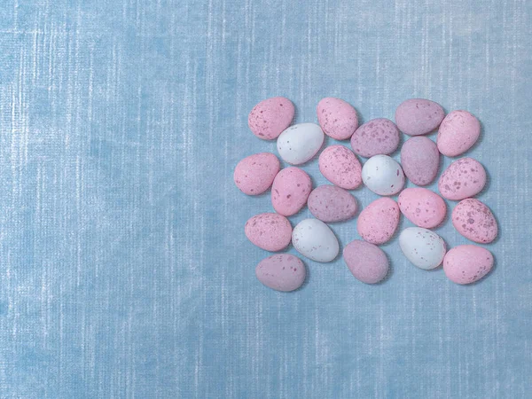 Pastel coloured mini eggs on the blue fabric. Easter concept copy space. High quality photo