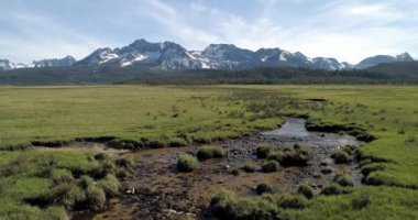 Arka planda testere dişli dağların olduğu ön planda bir dere manzarası