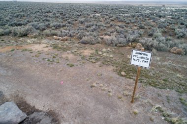 Çöl manzarasının geniş bir görüntüsü. Çöpe atılma cezasına dair bir uyarı içeriyor. Arazi seyrek, kuralları ve çevresel bakımı vurguluyor.
