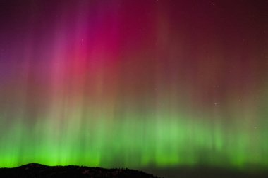 Muhteşem aurora borealis gece gökyüzünü canlı renklerle aydınlatıyor. Bu doğal mucize, yeşil ve kırmızı çarpıcı tonlarıyla evrenin güzelliğini gözler önüne seriyor..