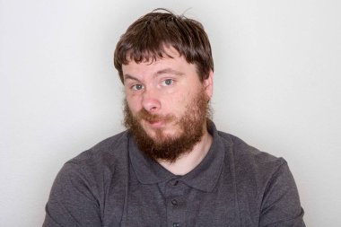 Gri gömlekli, düşünceli, sakallı bir adamın portresi. Meraklı bir şekilde bakıyor, tarafsız bir arkaplana karşı merakını ve içgörüsünü dile getiriyor. Düşünce teması için uygun