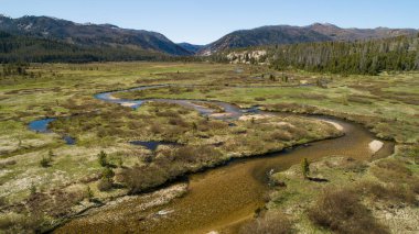 Berrak, mavi bir gökyüzü altında yemyeşil ve uzak dağlarla çevrili dolambaçlı bir nehrin bulunduğu sakin bir dağ vadisine nefes kesici bir hava manzarası.