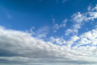 Sakin ve geniş mavi gökyüzü narin beyaz ve gri bulutlarla dolu, barışçıl ve açık bir atmosfer yaratıyor..