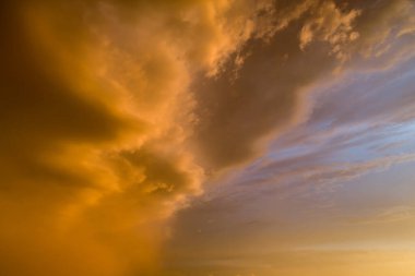 Gökyüzü turuncu ve bulutlu. Bulutlar alçak ve güneş batıyor. Gökyüzü turuncu ve mavinin karışımıdır.