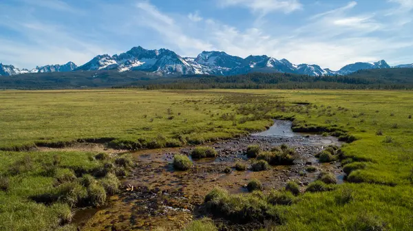Karla kaplı büyük bir dağ sırası uzaktan görülebilir. Gökyüzü açık ve mavidir, ve çimenlik alan küçük kayalarla doludur. Huzurlu ve huzurlu bir sahne.
