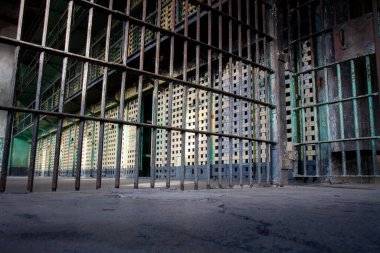 Metal çitli bir hapishane hücresi. Parmaklıklar paslı ve hücre boş. Manzara kasvetli ve kasvetli