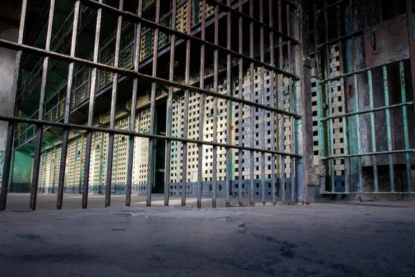 Metal çitli bir hapishane hücresi. Parmaklıklar paslı ve hücre boş. Manzara kasvetli ve kasvetli