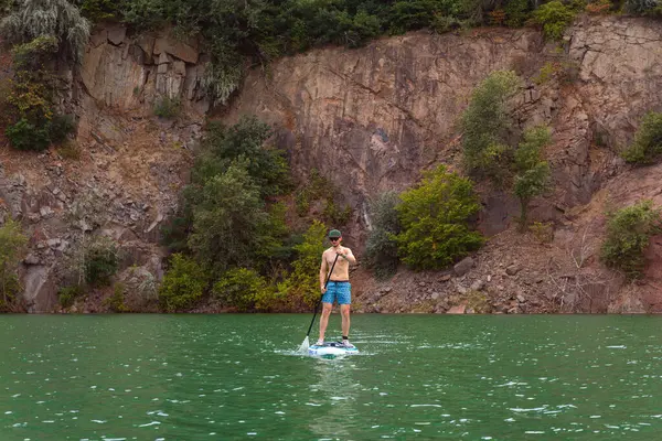 Aktif bir genç adamın yeşil zümrüt suyun üzerinde yüzerken çekilmiş fotoğrafları. Kırmızı renkli granit bir kayanın arka planına karşı.