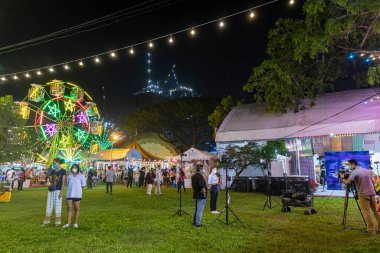 Bangkok, Tayland - 8 Aralık 2022: Arka planda dönme dolabı olan yerel bir muhabir bildiriyor. 8-18 Aralık 2022 tarihleri arasında Kızıl Haç Fuarı 'nda düzenlenecek. Görüntü hareketle bulanıklaşıyor.