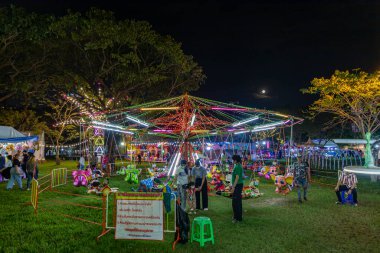 Bangkok, Tayland - 8 Aralık 2022: 8-18 Aralık 2022 tarihleri arasında Kızıl Haç Fuarı sırasında güzel aydınlatılmış bir eğlence parkına bir kalabalık girer. Görüntü hareketle bulanıklaşıyor..
