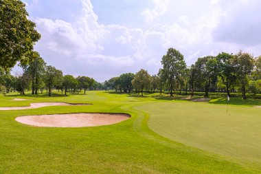 Tayland 'da yemyeşil çimlerle bezenmiş bir golf sahası yeşilliklerin ve golf deliklerinin yanında kum çukurları olan güzel bir manzara. Mavi gökyüzü güneşli gün.