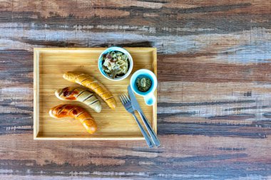 Küçük bir kasede lahana turşusu ve dijon hardalıyla mükemmel pişirilmiş ızgara Alman sosisi manzarası. Dikdörtgen bir ahşap tepside, ahşap bir masanın üzerinde, doğru kopya alanı var.