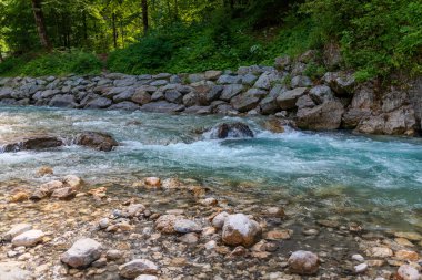 Bavyera 'nın Garmisch-Partenkirchen kentindeki bir orman yolunun yakınındaki pürüzsüz taşların üzerinden akan turkuaz suyla temiz bir alp deresi. Açık hava ve seyahat temaları için mükemmel huzurlu bir doğa sahnesi..