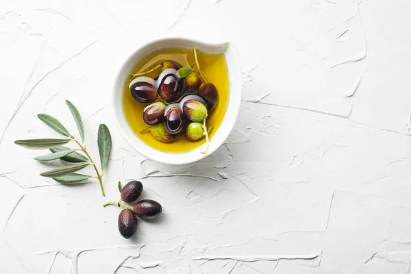 Olive oil in bowl with fresh olives fruit and olive branch on white background