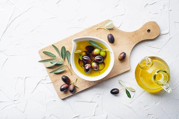 Olive oil in bowl with fresh olives fruit and olive branch on white background close up