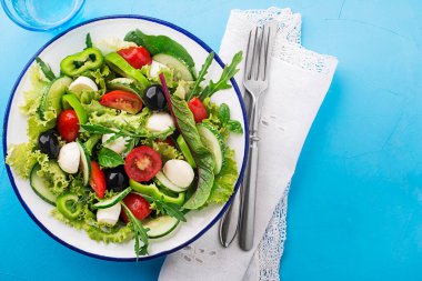 Green Salad with mozzarella cheese, black olives, arugula and tomato on blue table background
