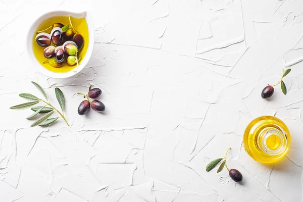 Olive oil in bowl and bottle with fresh olives fruit and olive branch on white background