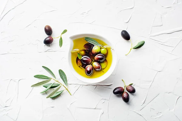 Olive oil in bowl with fresh olives fruit and olive branch on white background close up