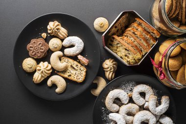 Tasty homemade sugar cookies and biscuits of all shapes and sizes on black table background
