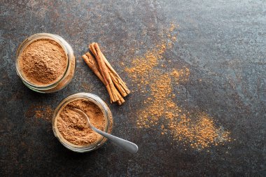 Ground cinnamon in glass cups and cinnamon sticks with powder on grey rustic background
