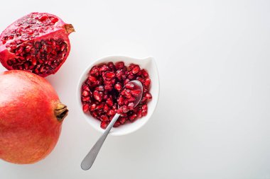 Healthy ripe pomegranate fruit opened and splited with seeds in cup on white background