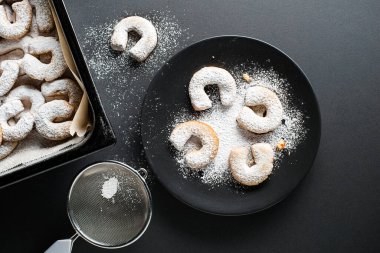 Baking Traditional vanilla crescents cookies and powdered with castor sugar. Holiday baking concept on black background clipart