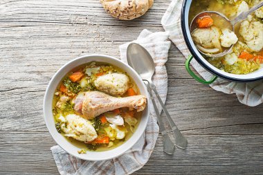 Fresh chicken soup with vegetable and semolina dumplings on wooden background overhead shoot