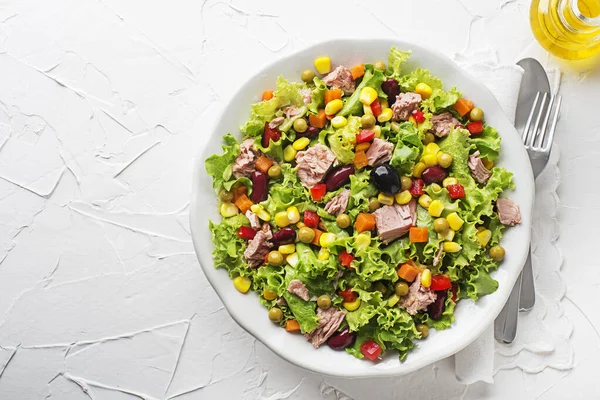 Healthy Green salad with tuna, corn, carrots, peas, peppers and olives on white table background. Mexican corn salad.