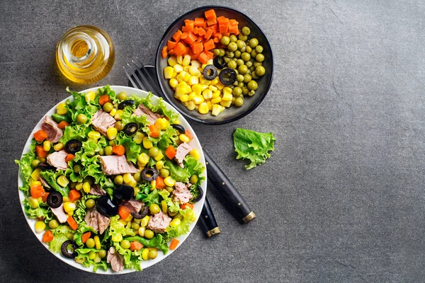 Healthy Green salad with tuna, corn, carrots, peas, and olives on grey table background. Mexican corn salad.