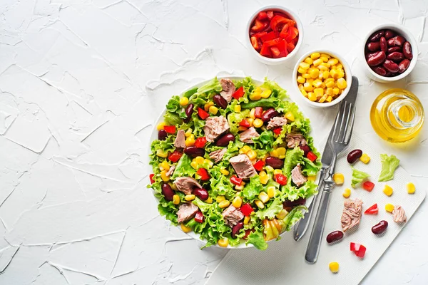 Healthy Green salad with tuna, corn, red pepper and beans on white table background. Mexican corn salad.