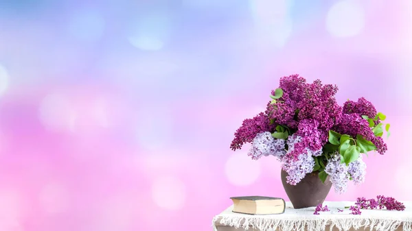 bouquet of lilacs in a vase on the table. On a blurred background in pink and blue, background and wallpaper for design and decoration with empty space for text