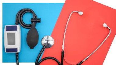 Kan basıncını ve nabız hızını ölçmek için elektronik tonometre ve steteskop. Kırmızı-mavi arka planda üst görüntü.