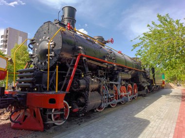 Müzedeki siyah Sovyet buharlı lokomotifi, ağaçların ve gökyüzünün arka planına karşı, yakın plan, yan görüş