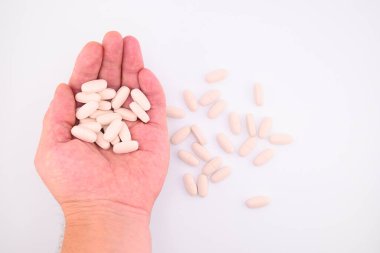 Bir avuç dolusu beyaz kapsül hapçısı elinde tutuyor, yakın plan, beyaz arka plan, üst görünüm.