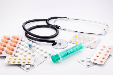 Stetoskop, su toplayan pakette büyük renkli haplar ve yeşil tek kullanımlık şırınga, yakın çekim, yan görüş.