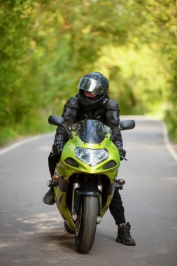 Motosikletli siyah koruyucu takım elbiseli ve kasklı yeşil spor bisikletli.