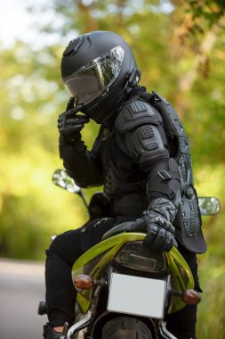 Siyah koruyucu takım elbiseli motosikletçi ve yeşil spor motosikletli kask, arka planda yeşil ağaçlar, arka manzara, yeşil bisiklet.