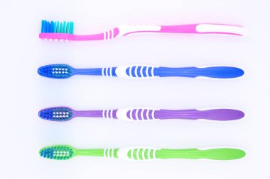Renkli diş fırçaları beyaz arkaplanda düzgün sıralanmış, her diş fırçasının günlük diş bakımına uygun eşsiz bir rengi ve tasarımı var, yakın plan, üst görünüm