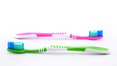 İki diş fırçası beyaz arka planda sıralanmış, biri yeşil, diğeri pembe, günlük diş ve ağız bakımı için uygun, yakın plan, yan görüş.