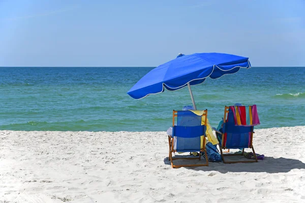白沙滩上有雨伞的蓝色海滩椅子 图库图片