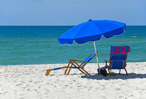 白沙滩上有雨伞的蓝色海滩椅子 图库照片
