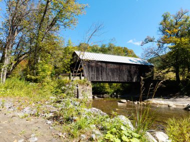 Tarihsel Moxley ahşabı, Chelsea, Vermont, ABD 'de yeşil yeşillikler ve mavi gökyüzünün ortasındaki kayalık bir dereyi kaplayan köprüyü kapladı..