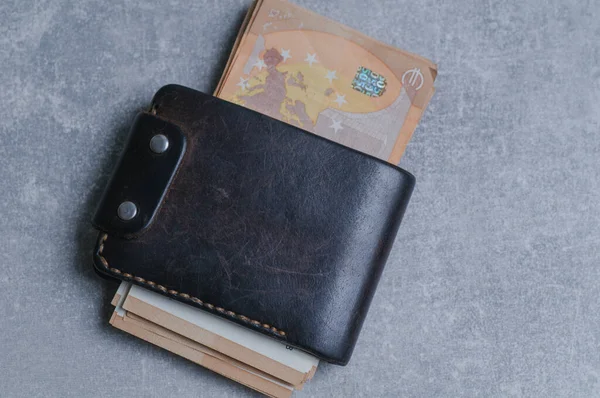 Black leather wallet with a stack of books and credit cards on a gray background