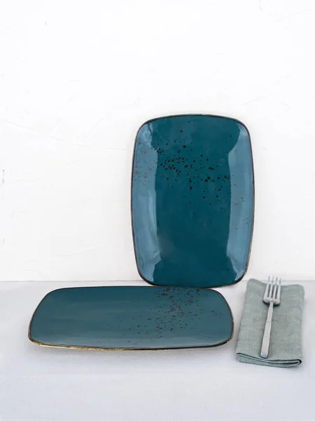 两个空的蓝色矩形餐盘 桌布铺在白底桌布上 桌布上有两个带有叉子的蓝色手工陶瓷盘 免版税图库照片