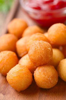Fresh round baked Duchess potatoes or croquettes on wooden board, ketchup in the back (Very shallow depth of field, Focus on the potato balls in the front)
