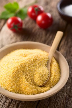 Raw coarsely ground cornmeal or polenta on wooden plate with wooden spoon (Selective Focus, Focus one third into the plate)